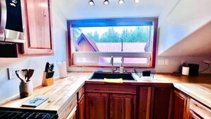 Cucina con mobili in legno, cappa aspirante in acciaio inossidabile, finestra con vista su una casa e piano di lavoro con lavello e diversi oggetti da cucina.