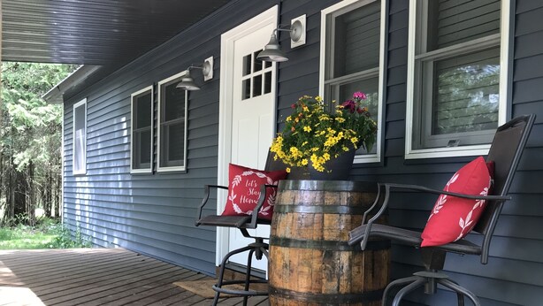 A wooden deck with a metal barrel planter and two chairs with red cushions. - Whitetail Hollow  (McBain)