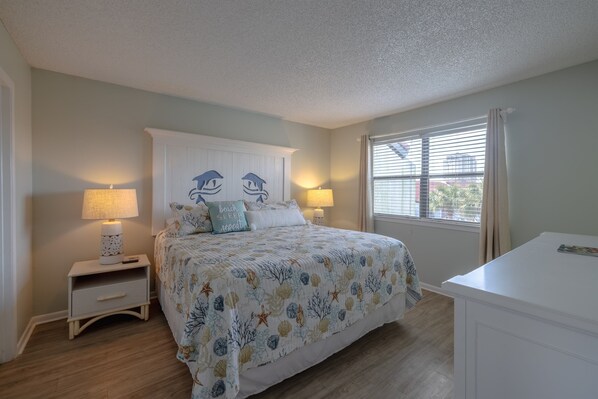 A bedroom with a bed, two bedside tables with lamps, a nightstand, a dresser, and a window with curtains.