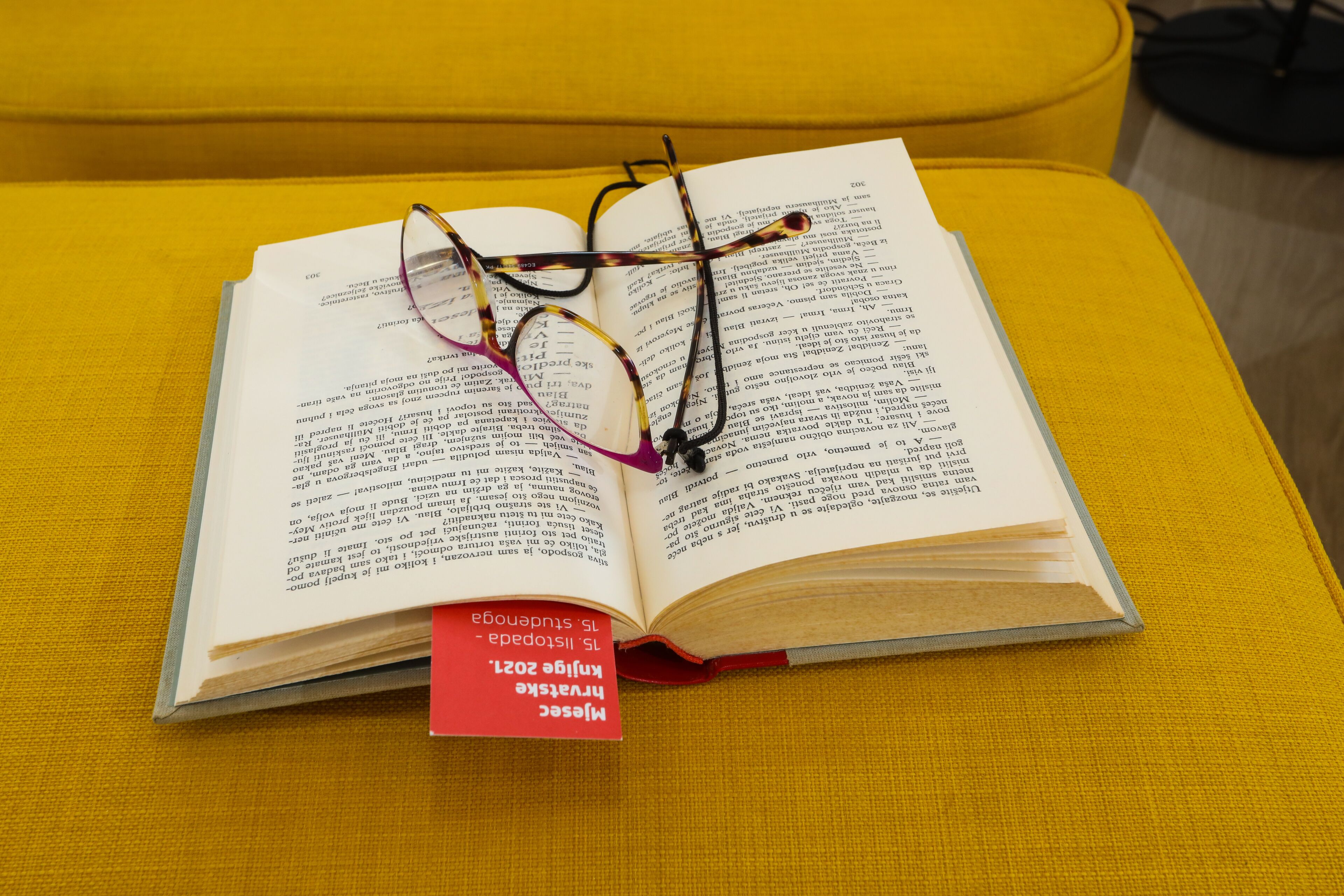 An open book with glasses on top, placed on a yellow cushion.