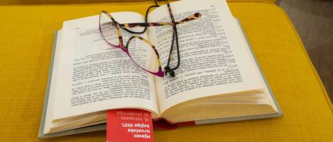 An open book with glasses on top, placed on a yellow cushion.