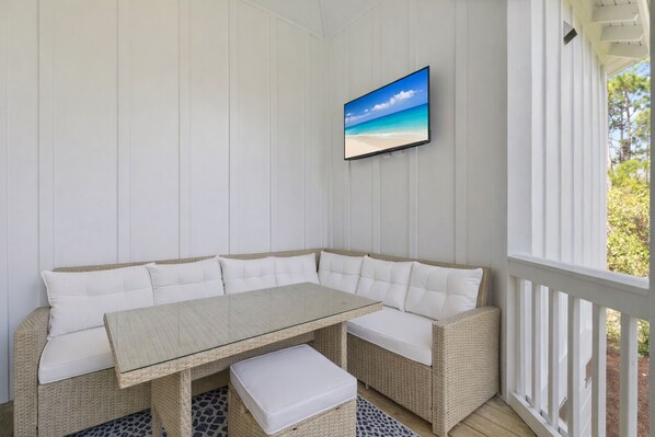 A covered outdoor seating area with a glass-top table and white cushioned benches.