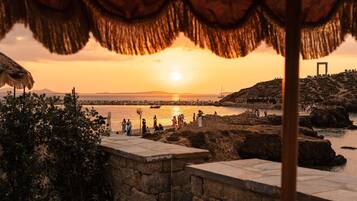 A sunset view from a stone balcony overlooking a beach with people and a sailboat.