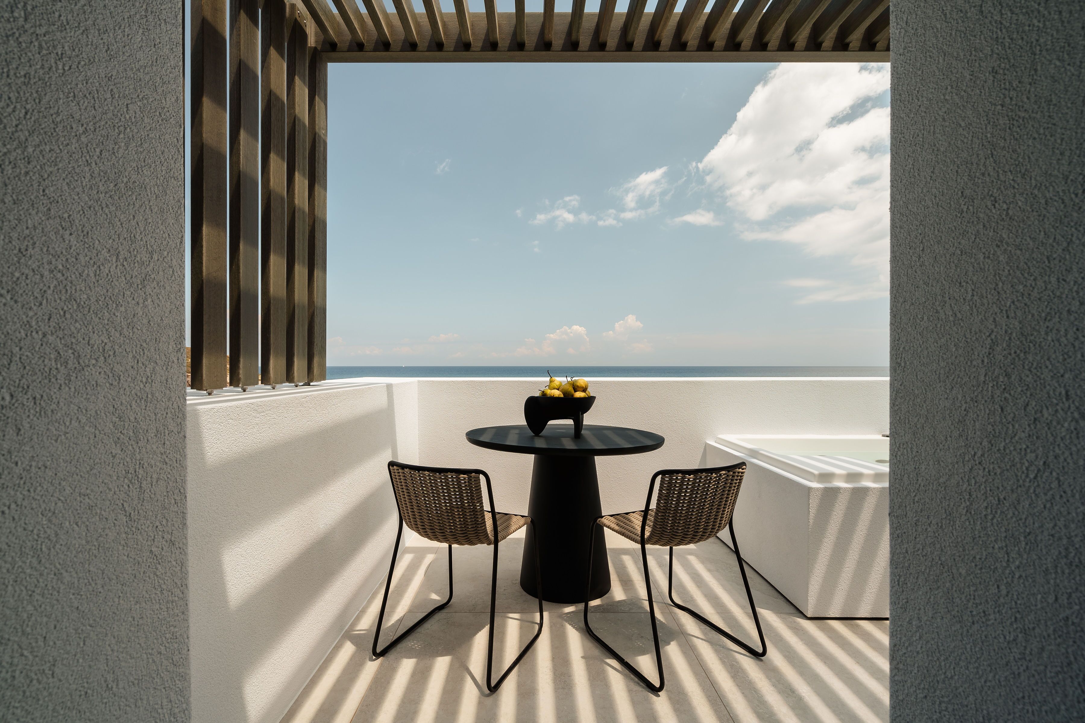 A balcony with a round table and two chairs, overlooking a beach.