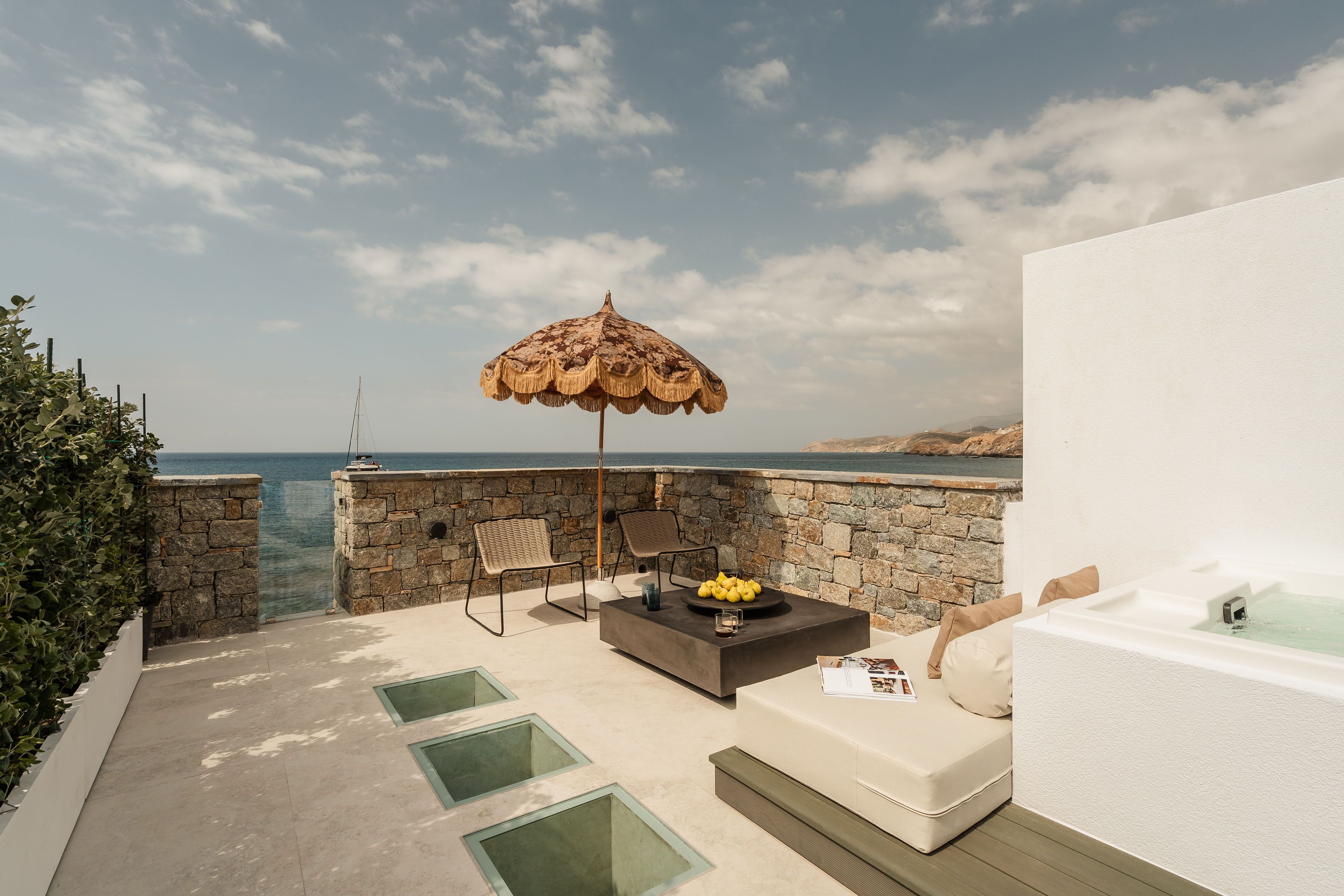 A modern outdoor lounge area with a stone wall, a large umbrella, a fire pit, and a hot tub.