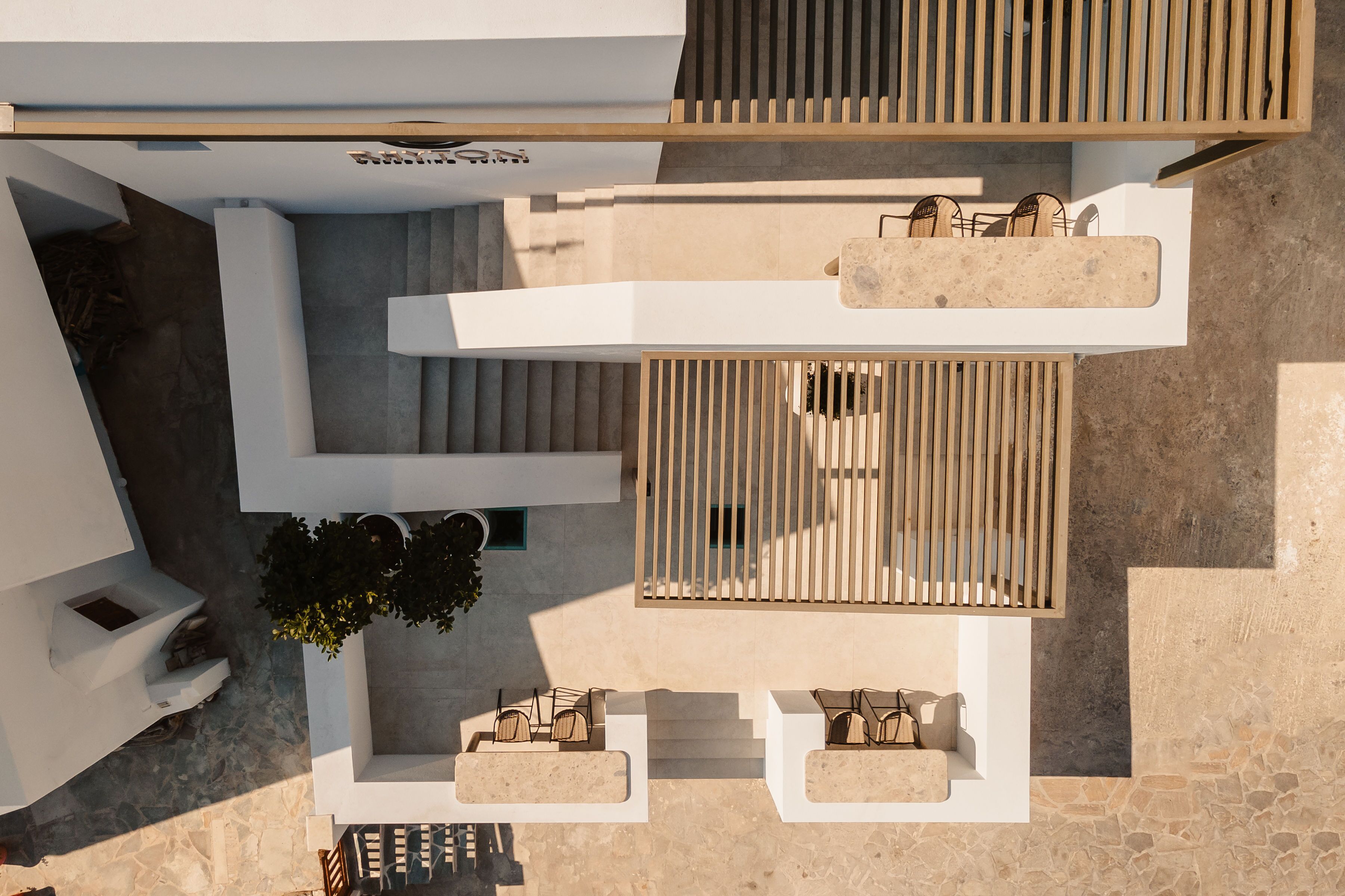 An aerial view of a modern building with a rooftop terrace, outdoor seating area, and a staircase leading to an upper level.