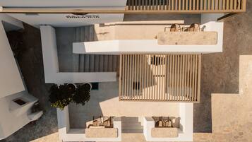 An aerial view of a modern building with a rooftop terrace, outdoor seating area, and a staircase leading to an upper level.
