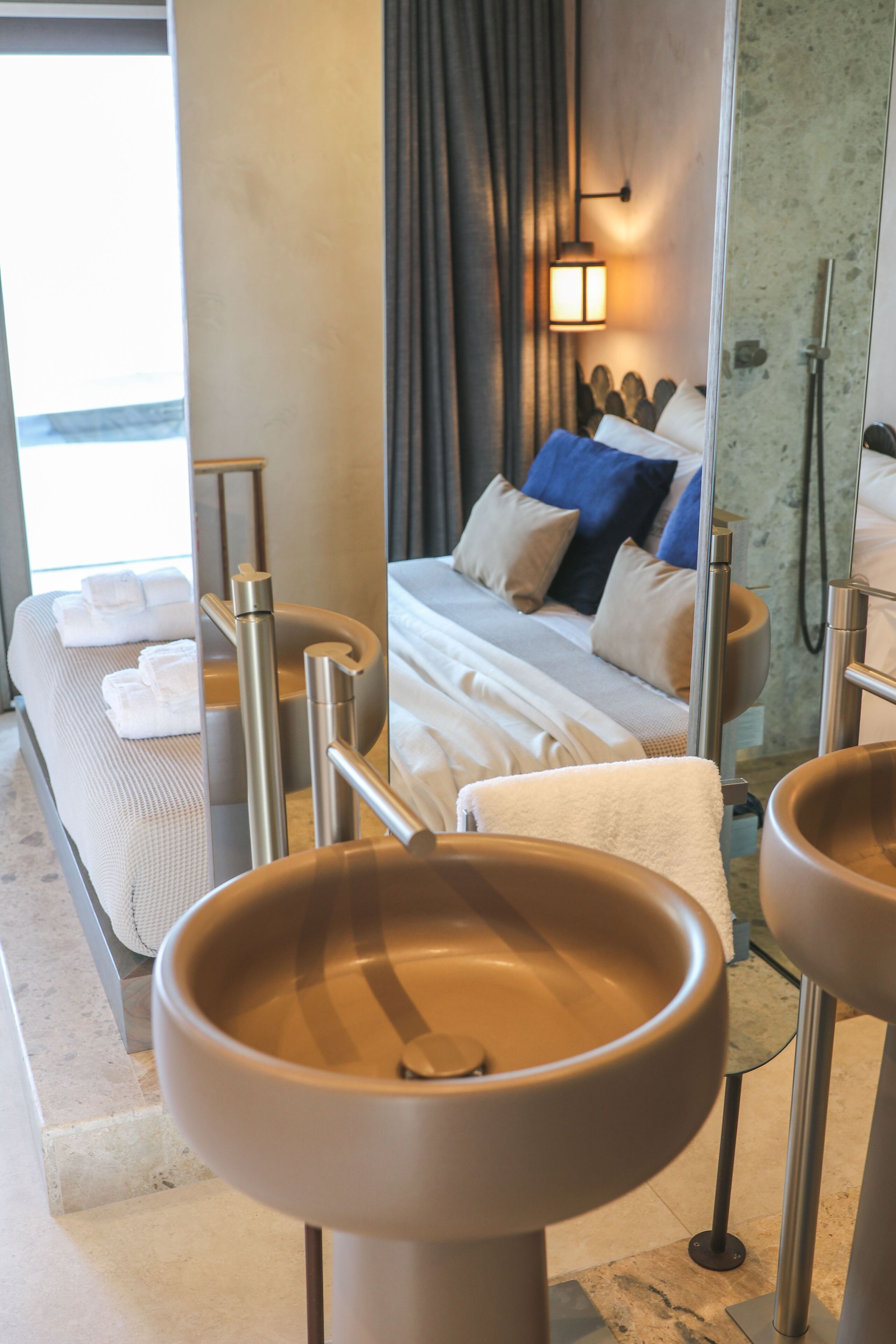 A hotel room with a bed, bedside tables, a large mirror, and a view of the sea.