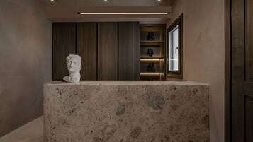 Un baño moderno con encimera de mármol, una escultura de busto blanco, paneles de madera y estantes empotrados con objetos decorativos.