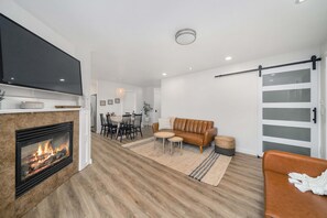 Un salon moderne doté d’une cheminée, d’un téléviseur à écran plat, d’un canapé en cuir marron et d’un coin repas avec des chaises et une table.