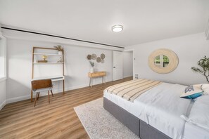 Une chambre moderne avec un plancher en bois, un lit doté d  ’une tête de lit grise, un bureau blanc et un miroir rond accroché au mur.