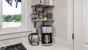 A kitchen with a coffee maker, a kettle, and shelves with jars and cups.