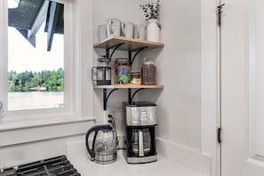 Une cuisine équipée d’une machine à café, d’une bouilloire et d’étagères remplies de bocaux et de tasses.