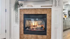 A modern fireplace with a digital clock, a plant, and a kitchen in the background.