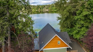 A cabin with a green garage, surrounded by trees and a lake.