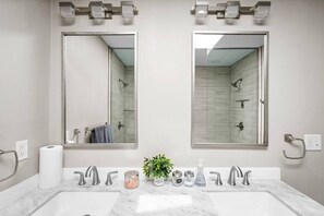 Ample natural light illuminates the bathroom, featuring a large mirror, marble countertop, and a single sink.