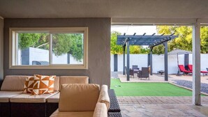 Ein überdachter Patio-Bereich mit einer Couch, einer Pergola und Gartenmöbeln.