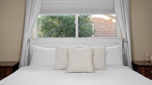 Ein ordentlich bezogenes Bett mit weißer Bettwäsche und einem Fenster mit weißen Vorhängen.