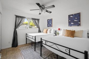 Two single beds with white bedding and pillows, a ceiling fan, and a large window with curtains.