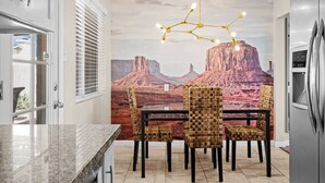 Une cuisine moderne avec un coin repas, agrémentée d’une fresque représentant un paysage de montagne, d’un lustre et d’un réfrigérateur.