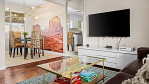 Un salon moderne doté d’un grand téléviseur à écran plat, d’une table basse en verre et d’une fresque représentant un paysage désertique.
