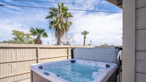 Un bain à remous installé à l’extérieur, entouré d’une clôture en bois et avec des palmiers en arrière-plan.