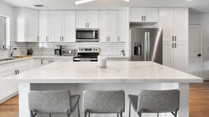 Cozinha moderna com armários brancos, uma ilha grande com banquetas, eletrodomésticos de aço inoxidável e um ventilador de teto.