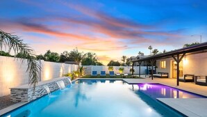 Piscina com cascata, rodeada por espreguiçadeiras e uma área de estar coberta.