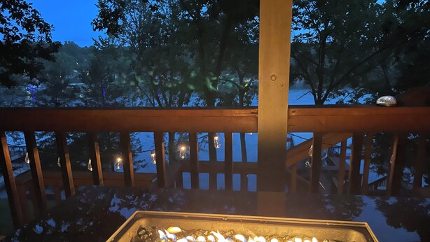 A fire feature with a metal frame and a glass enclosure, surrounded by a wooden deck with railings and string lights. - Lakeside Dreaming! 2b-2b, Sleeps 6, Lake of the Ozarks. (Gravois Mills)