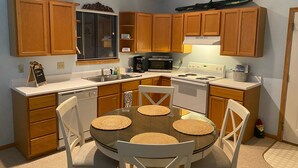 A compact kitchen with wooden cabinets, a microwave, stove, and a dining table with placemats. - Lakeside Dreaming! 2b-2b, Sleeps 6, Lake of the Ozarks. (Gravois Mills)