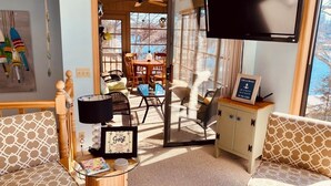 A cozy living room with a sofa, a wooden cabinet, and a television. There is a dining area with chairs and a table visible through a glass door. - Lakeside Dreaming! 2b-2b, Sleeps 6, Lake of the Ozarks. (Gravois Mills)