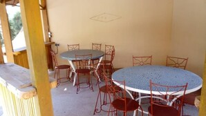 Un patio exterior techado con una mesa redonda y sillas de metal rojas.