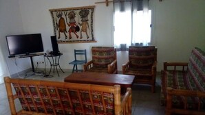 Una sala de estar con una televisión, dos sillones estampados, un sofá de madera y una mesa.