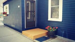 Uma casa azul com porta preta, janela branca e um vaso com flores vermelhas.