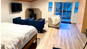 Un dormitorio con una cama, un sofá azul, una silla, una chimenea y un ventanal con vistas a árboles.