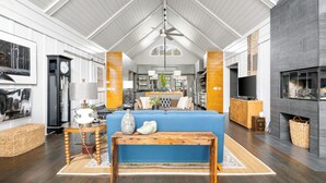 A spacious living area with a high ceiling, a fireplace, and a large blue sofa. - Hemingway | Jungle Hideaway (Folly Beach)