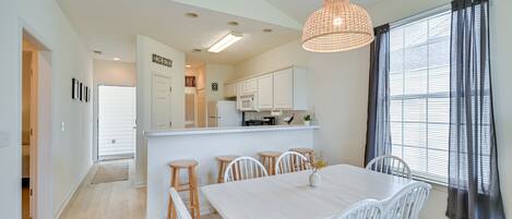 A modern kitchen with white cabinets, a central island, and a dining area with a white table and chairs.