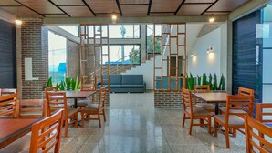 A modern dining area with wooden tables and chairs, a brick wall, and a staircase leading to an upper level.