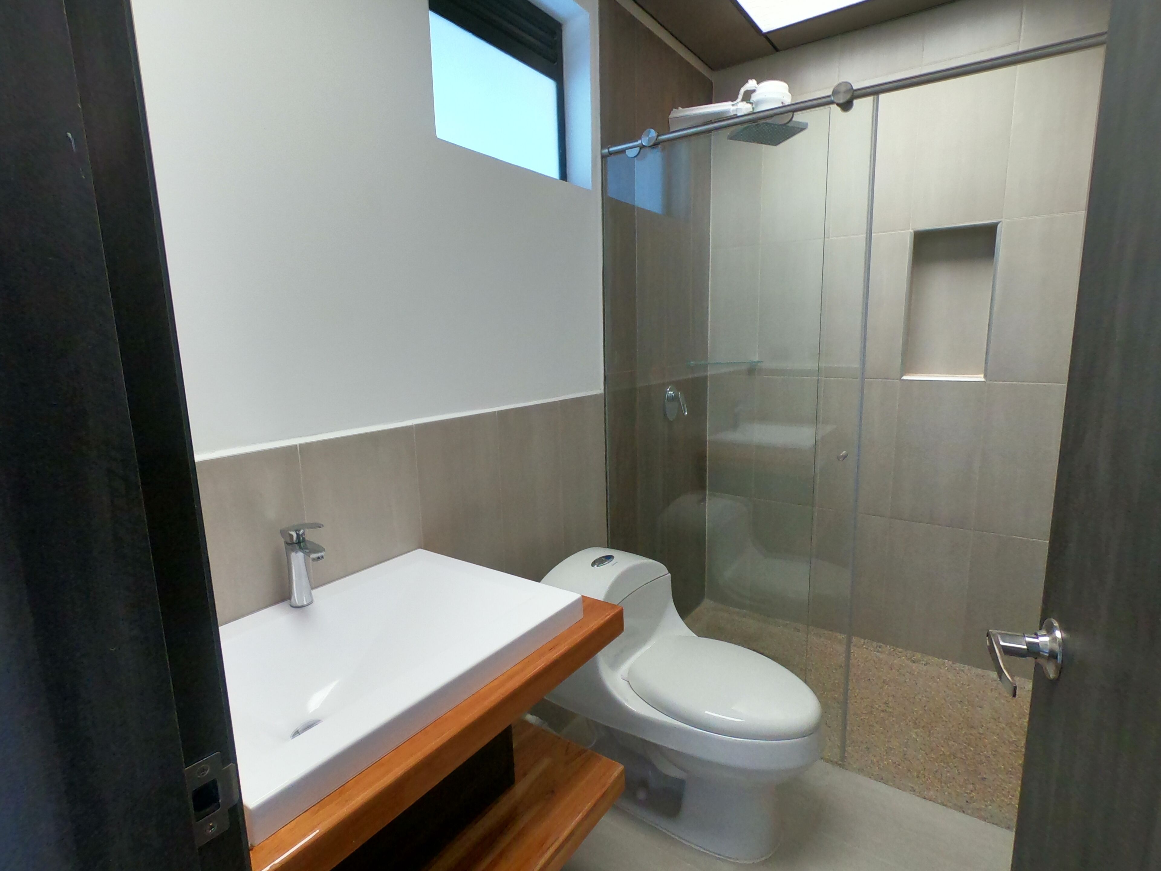 A modern bathroom with a glass shower enclosure, a white toilet, and a wooden vanity.