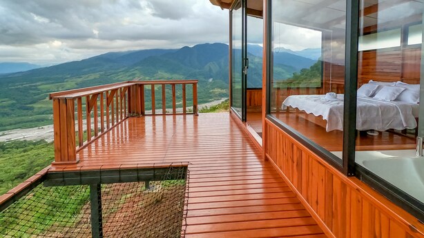 A wooden deck with a glass balustrade overlooking a mountainous landscape.