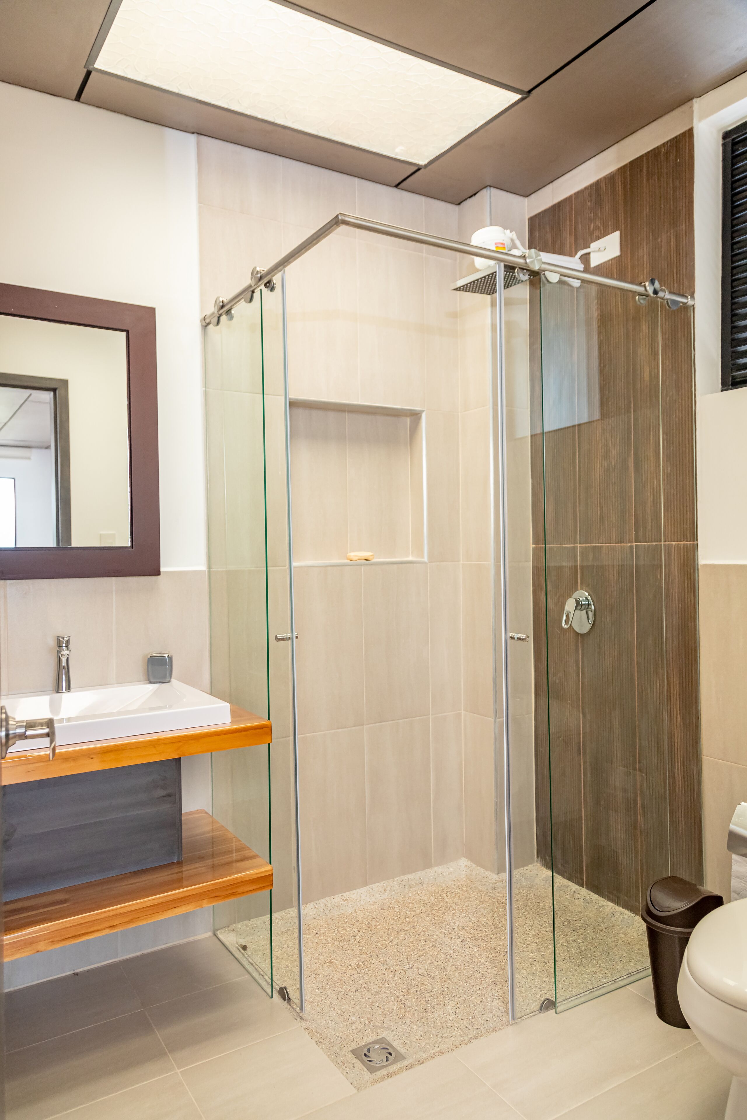 Un baño moderno con ducha de vidrio, tocador de madera y un espejo grande.