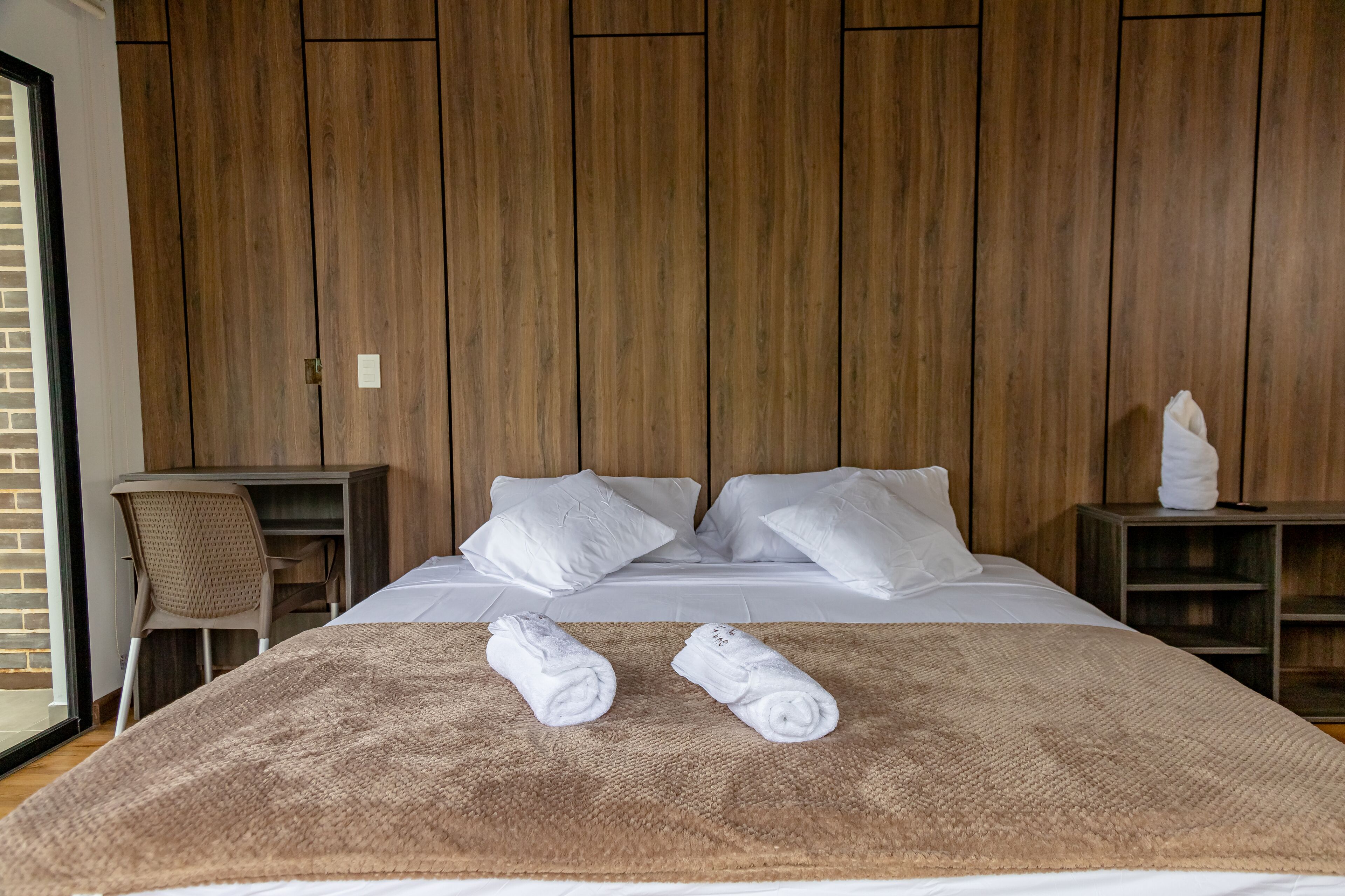 Een hotelkamer met een groot bed, twee witte kussens, een bruine deken en twee opgerolde handdoeken.