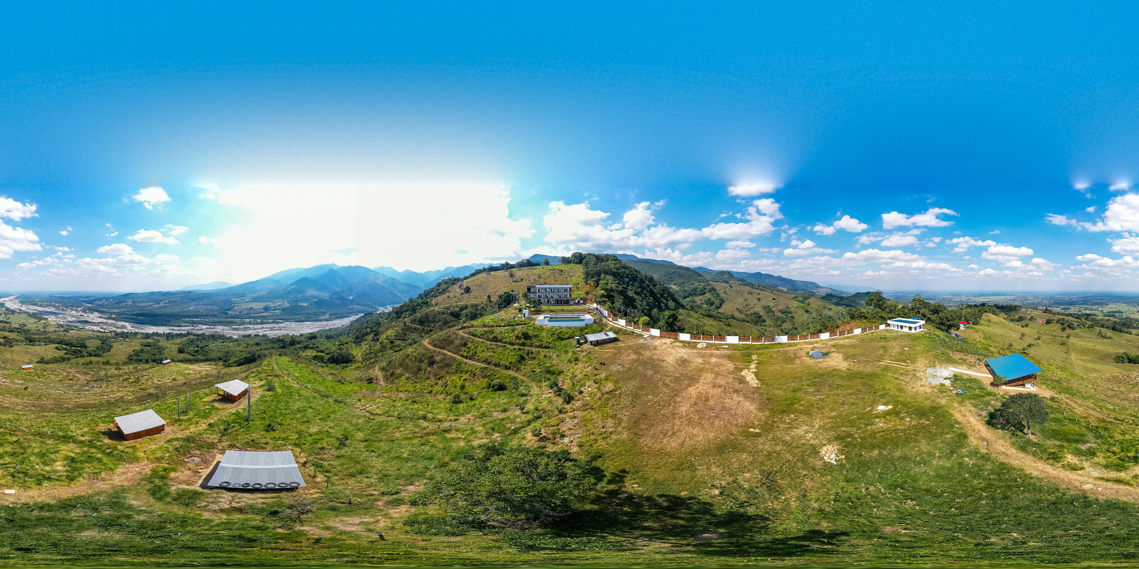 Une vue panoramique d’un paysage rural, avec une colline imposante, plusieurs petits bâtiments et un ciel bleu dégagé.