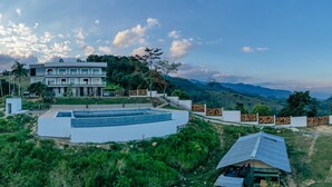 A modern house with a swimming pool, surrounded by lush greenery and mountains.