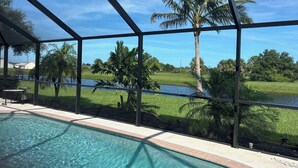 Zona de piscina con vistas a un río y palmeras, delimitada por una estructura metálica.