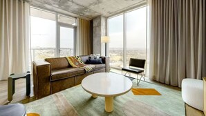Quarto de hotel moderno com uma janela ampla, um sofá, uma mesa redonda e vista para a cidade.