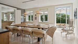 A spacious dining area with a large wooden table and multiple chairs, large windows with curtains, and a view of the outdoors. - 4 bedroom nice home in Nyborg (Nyborg)