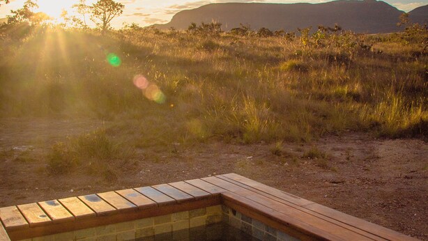 Een hottub met een houten terras, omgeven door een natuurlandschap met gras en bergen op de achtergrond.
