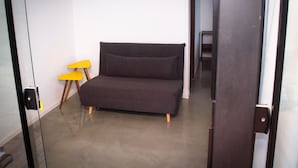 Een compacte kamer met een donkergroene bank, een kleine gele stoel, en een deur naar een andere kamer.