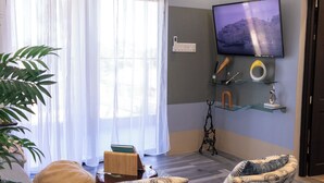 A living room with a television mounted on the wall, a plant, a sofa, and a small table. - Villa on the Rock ~ Luxury vacation rental near beach with Roof top lounge area (Trelawny)